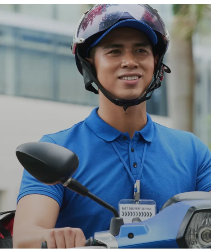 Smiling delivery rider in a blue polo and helmet on a blue scooter, wearing an ID badge