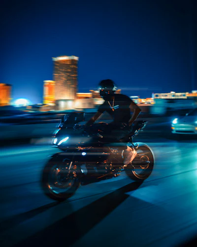 Motorcyclist riding along a waterfront at night with city lights behind