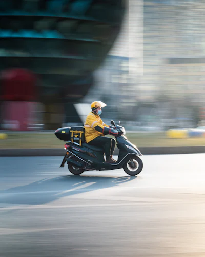 Rider in a yellow jacket on a scooter with a delivery box